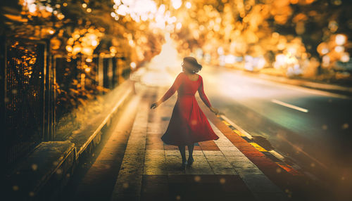 Rear view of woman walking on footpath at night