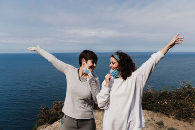 Lesbian couple standing by sea against sky