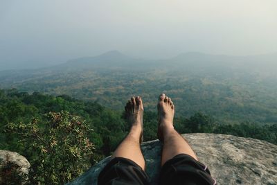 Low section of man sitting on mountain against sky