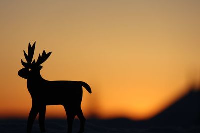 Silhouette deer standing on land against sky during sunset