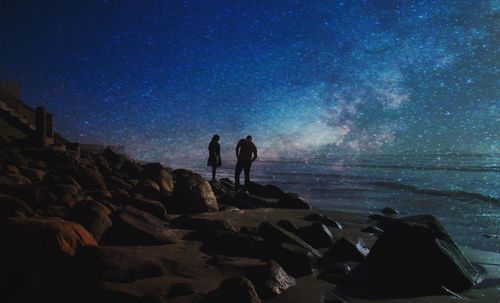 People standing on rock at beach against sky