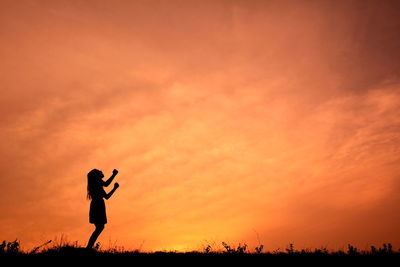 Silhouette of woman punching air at sunset