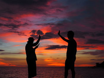 Silhouette people on beach against dramatic sky during sunset