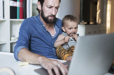 Mid adult businessman using laptop while taking care of baby at home