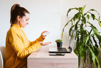 Side view of woman using phone while sitting on table