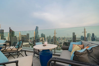 Empty chairs and tables against buildings in city against sky