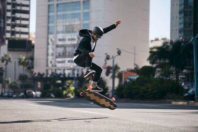 Full length of man performing stunt while skateboarding on road in city