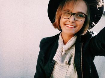 Smiling woman wearing eyeglasses and hat against wall