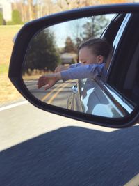 Reflection of boy looking through car window on side-view mirror