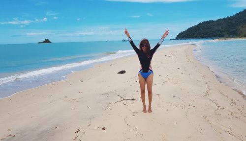 Portrait of smiling woman with arms raised standing on beach