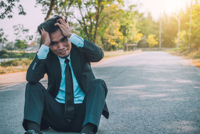 Full length of man sitting on road against trees