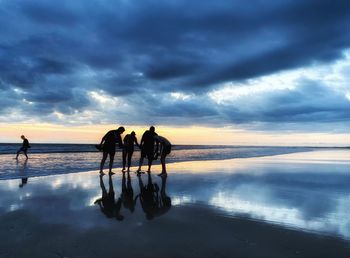 People standing on beach against sky during sunset