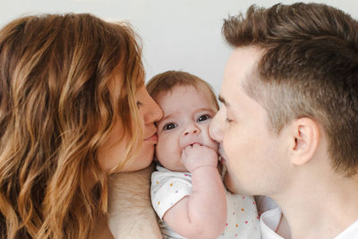 Cheerful mother and father kissing daughter at home