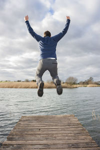 Full length rear view of man jumping against sky