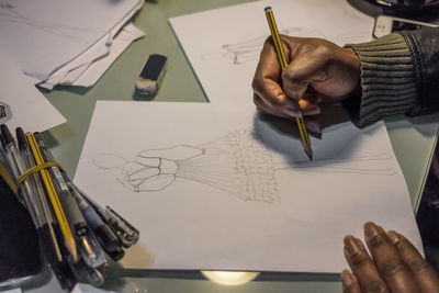 Cropped hands of female fashion designer drawing on paper at desk