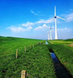 Scenic view of agricultural field against sky with wind turbine as backdrop. 