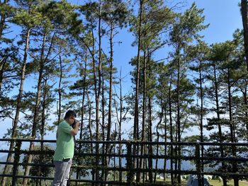 Low angle view of woman standing by trees in forest against sky