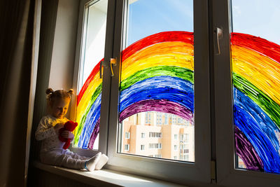 Little girl on background of painting rainbow on window. kids leisure at home. 