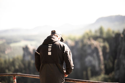 Rear view of man standing by railing against sky