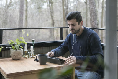 Man with headphones using digital tablet while sitting at table in balcony