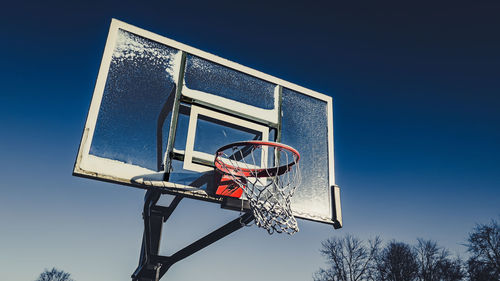 Basketball hoop splattered with snow with blue sky above.