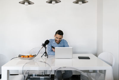 Businessman with microphone using laptop while sitting by table at home