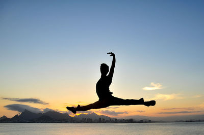 Silhouette man jumping above sea against sky during sunset