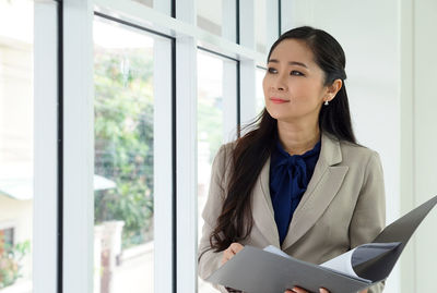 Smiling businesswoman holding file looking away through window