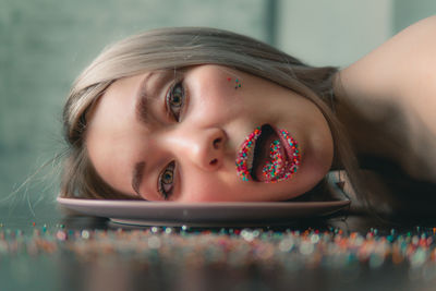 Close-up portrait of young woman with sprinkles on lips lying on plate