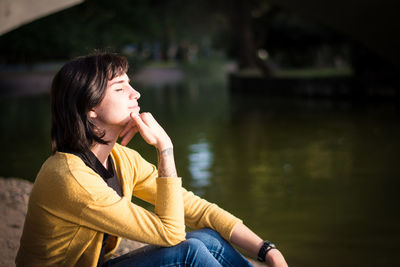 Young woman looking away while sitting by lake