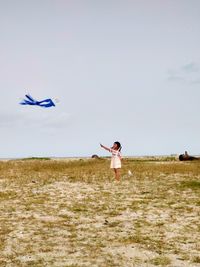 Full length of girl flying kite while standing on grass against sky