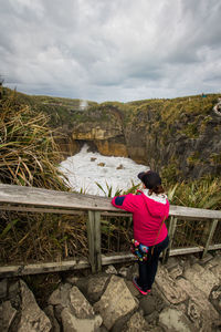 Rear view of woman standing on steps by flowing water against cloudy sky