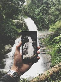 Midsection of man using mobile phone against trees