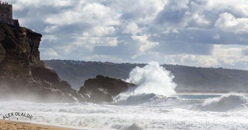 Waves splashing on rocks against sky