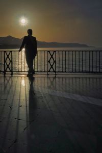 Silhouette man standing by railing against sea during sunset