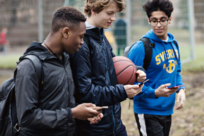 Friends using smart phones while walking on street after basketball practice