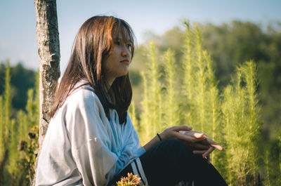 Side view of young woman sitting on field holding a smartphone, she look sad