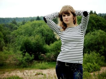 Portrait of woman with hand in hair standing against trees in forest