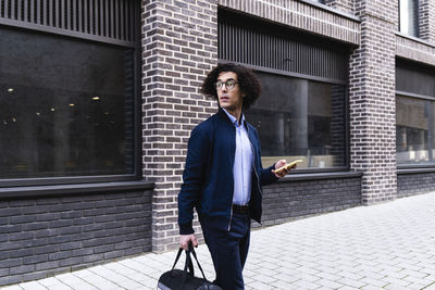 Man holding bag and mobile phone walking on footpath