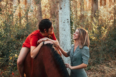 Woman sitting on horse while standing with friend