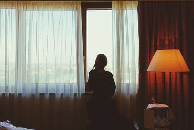 Rear view of woman by window at home