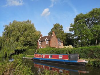 Boat moored on canal by trees and building against sky