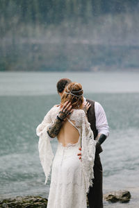 Two happy people in love the bride and groom in wedding outfits embrace by the lake and mountains