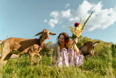 Smiling woman enjoying nature with goats and flowers on a sunny day