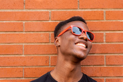 Smiling young man wearing sunglasses against brick wall