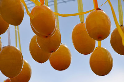 Low angle view of wooden easter eggs hanging from ribbons against sky