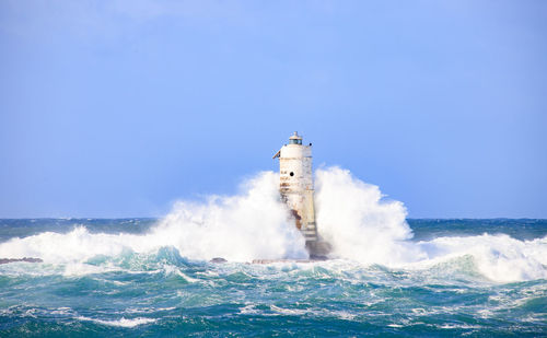 Lighthouse by sea against clear blue sky