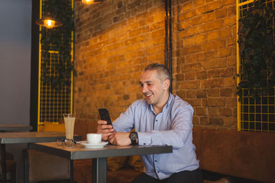 Young man using phone while sitting on table