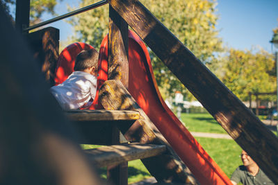 Baby boy playing on outdoor play equipment with father at playground