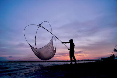 Silhouette fisherman on beach against sky during sunset